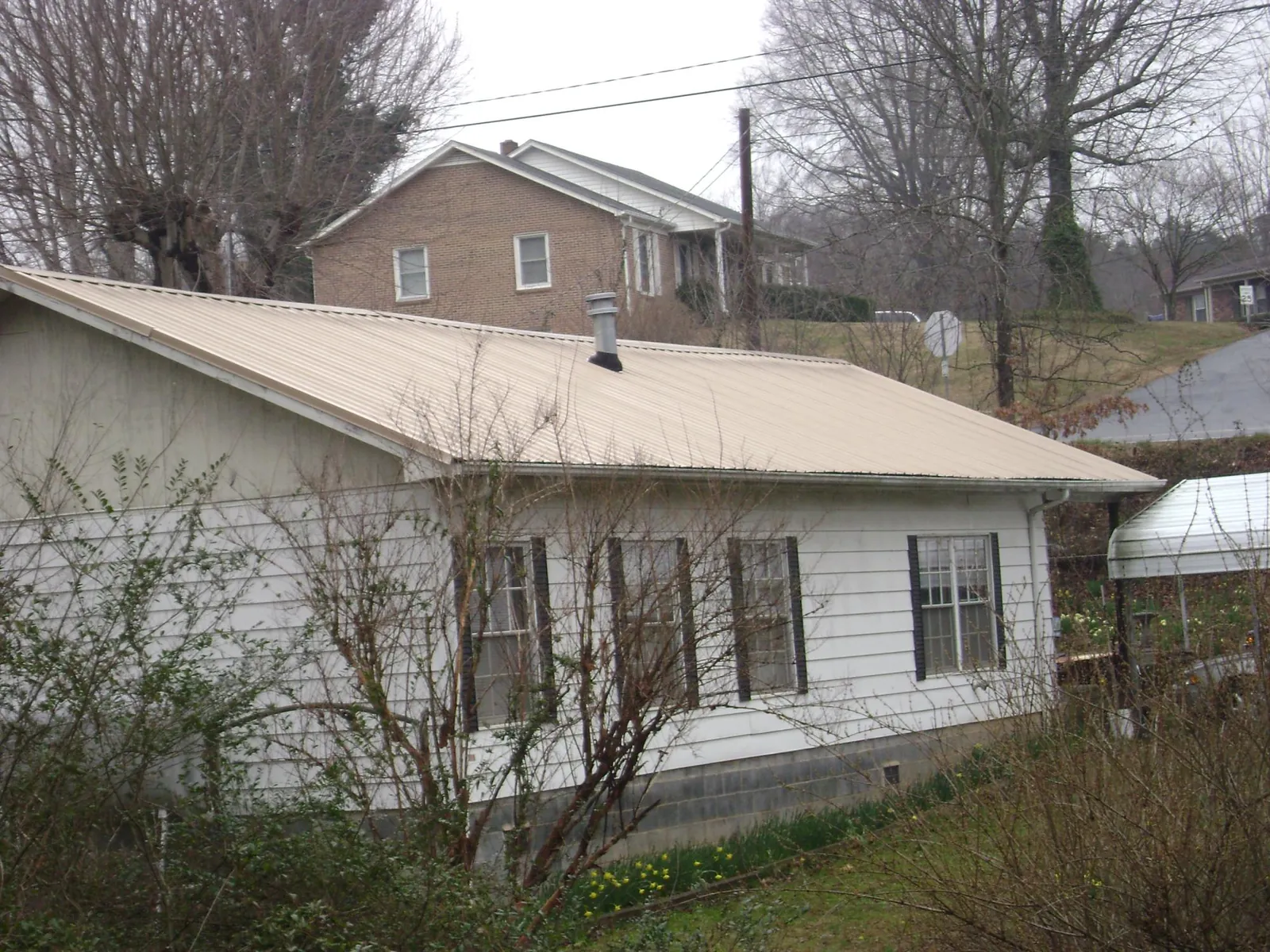 Tan metal roof on a white sided house set into a hillside — Commercial Roofing by Roofing Brothers in Mead